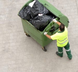 Worker pushing a dumpster manually in need of a motorized dumpster mover